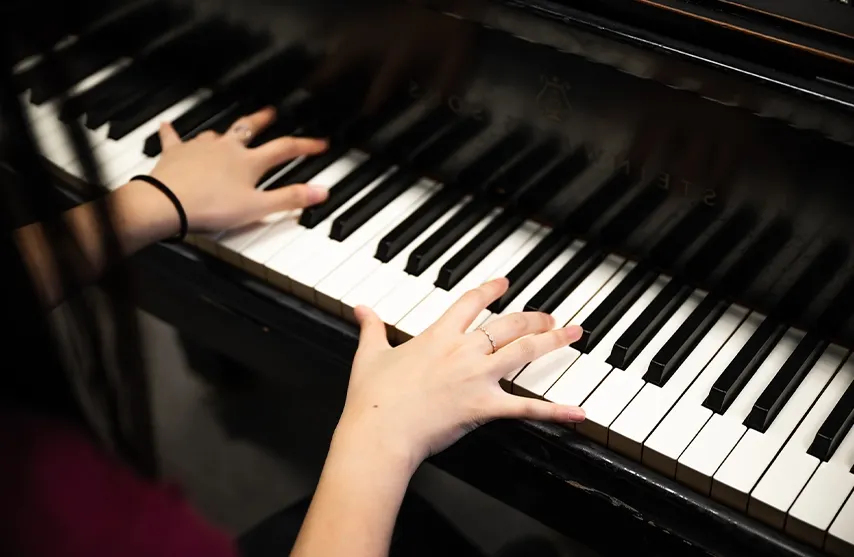 A close-up of a woman playing the keys of a black piano.